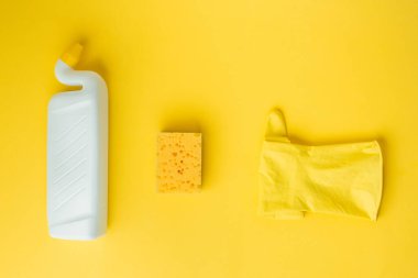 Sarı lastik eldivenler, baş parmakları kıvrılmış jest ve sarı arka planda beyaz, boş bir deterjan şişesi. Düz yatıyordu. Temizlik şirketi reklamı.