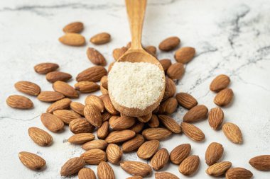 Tahta kaşık dolusu badem unu ve kurutulmuş badem tohumları. Beyaz mermer arka planda badem. Fransız tatlı kurabiyeleri için gerekli malzemeler. Sağlıklı beslenme konsepti. Düz yatıyordu