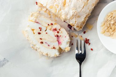 Beyaz mermer arka planda badem gevreği ve dondurulmuş kırmızı böğürtlenlerle süslenmiş ev yapımı kremalı pasta dilimi. Parşömen kağıdında krem şantili krema.