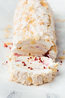 Beyaz mermer arka planda badem gevreği ve dondurulmuş kırmızı böğürtlenlerle süslenmiş ev yapımı kremalı pasta dilimi. Parşömen kağıdında krem şantili krema.