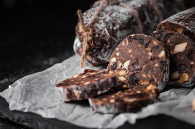 Badem, fındık ve siyah arka planda kuru üzümle dolu çikolatalı salam. Pudra şekeri serpiştirilmiş İtalyan tatlı sosisi. Noel ve Yeni Yıl Pastası