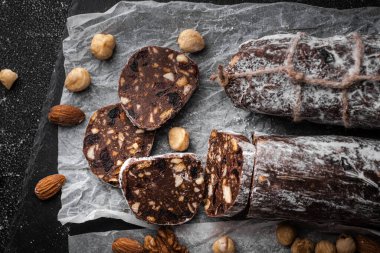 Badem, fındık ve siyah arka planda kuru üzümle dolu çikolatalı salam. Pudra şekeri serpiştirilmiş İtalyan tatlı sosisi. Noel ve Yeni Yıl Pastası