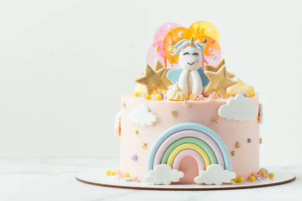 Unicorn cake with pink cream cheese frosting decorated with mastic rainbow, multicolored caramel candies and unicorn shaped figure on top. Birthday cake for a little girl on the white background