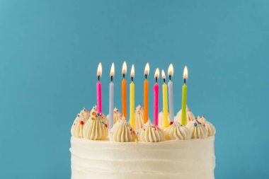 Mavi arka planda çok renkli mumlarla süslenmiş beyaz krem peynirli doğum günü pastası. Mutlu Yıllar konsepti.