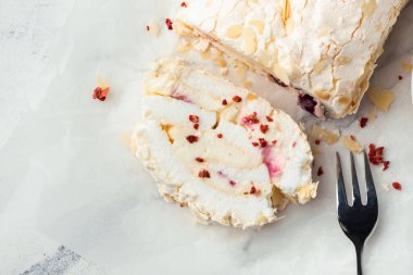 Beyaz mermer arka planda badem gevreği ve dondurulmuş kırmızı böğürtlenlerle süslenmiş ev yapımı kremalı pasta dilimi. Parşömen kağıdında krem şantili krema.