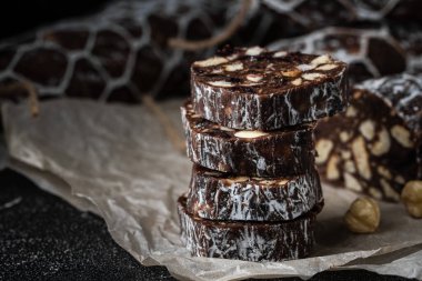 Badem, fındık ve siyah arka planda kuru üzümle dolu çikolatalı salam. Pudra şekeri serpiştirilmiş İtalyan tatlı sosisi. Noel ve Yeni Yıl Pastası