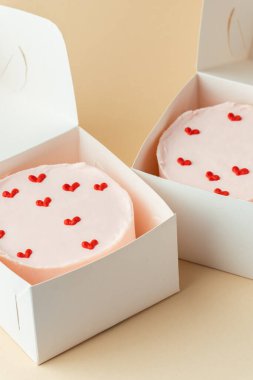 Bej arka planda beyaz bir kutuda kalpleri olan küçük Kore usulü pembe bento pastası. Sevdiğinin doğum günü hediyesi olarak hamur işi. Sevgililer Günü hediyesi.
