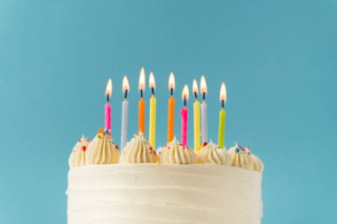 Mavi arka planda çok renkli mumlarla süslenmiş beyaz krem peynirli doğum günü pastası. Mutlu Yıllar konsepti.