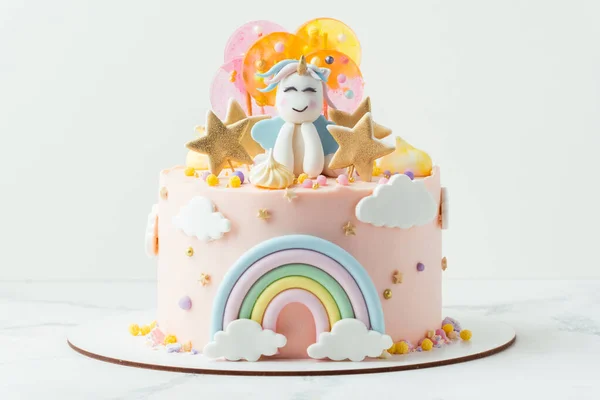 上有粉红奶油芝士糖霜的独角兽蛋糕 上面装饰着乳酪彩虹 五颜六色焦糖糖果和独角兽形的身影 白色背景的小女孩的生日蛋糕 — 图库照片