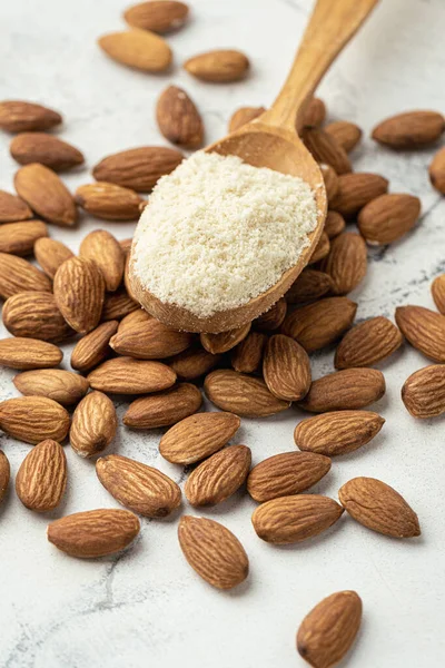 Wooden spoon full of almond flour on dried almond seeds. Almonds on the white marble background. Ingredient for French dessert macaroons. Healthy nutrition concept. Flat lay