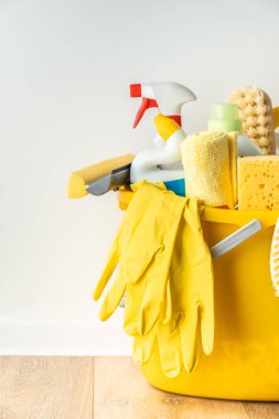 Fırçalar, temizleme sıvıları, süngerler, bez parçaları ve beyaz arka planda sarı lastik eldivenler. Ahşap zemindeki sarı kovadaki temizlik malzemeleri. Temizlik şirketi reklamı