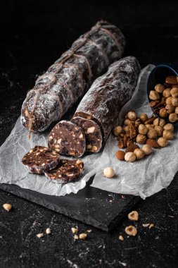Badem, fındık ve siyah arka planda kuru üzümle dolu çikolatalı salam. Pudra şekeri serpiştirilmiş İtalyan tatlı sosisi. Noel ve Yeni Yıl Pastası