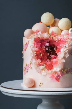 Koyu gri arka planda altın taç yapraklarıyla süslenmiş pembe krem peynirli lüks yıldönümü pastası. Sevgililer Günün kutlu olsun. Kırmızı ve pembe yenebilir kristalleri olan sevgili kadın için pasta.