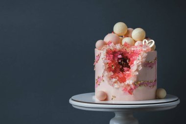 Koyu gri arka planda altın taç yapraklarıyla süslenmiş pembe krem peynirli lüks yıldönümü pastası. Sevgililer Günün kutlu olsun. Kırmızı ve pembe yenebilir kristalleri olan sevgili kadın için pasta.