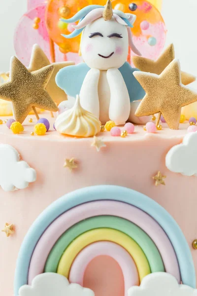 Unicorn cake with pink cream cheese frosting decorated with mastic rainbow, multicolored caramel candies and unicorn shaped figure on top. Birthday cake for a little girl on the white background