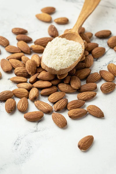Wooden spoon full of almond flour on dried almond seeds. Almonds on the white marble background. Ingredient for French dessert macaroons. Healthy nutrition concept. Flat lay
