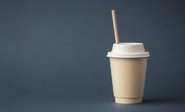 Coffee in a disposable paper cup with a straw on a gray background. Unbranded recycled paper cup with a copy space for a free text. Mockup. Care for the environment. Recycling or eco-friendly concept