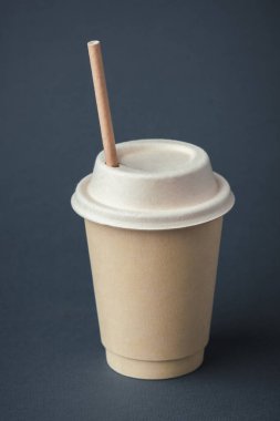 Coffee in a disposable paper cup with a straw on a gray background. Unbranded recycled paper cup with a copy space for a free text. Mockup. Care for the environment. Recycling or eco-friendly concept