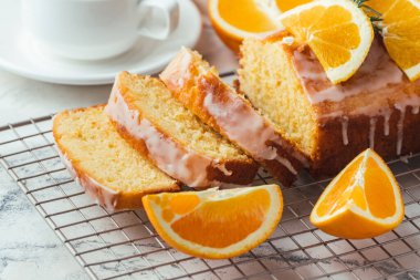 Loaf of orange bread covered with a confectionery glaze with lemon juice and decorated with orange slices. Chiffon cake on a pastry grill next to cup of tea. White background