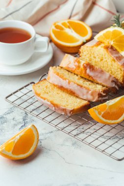 Loaf of orange bread covered with a confectionery glaze with lemon juice and decorated with orange slices. Chiffon cake on a pastry grill next to cup of tea. White background