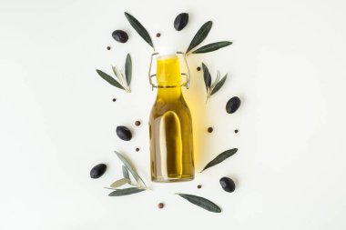 Green and black olives in white bowls next to a bottle with olive oil and leaves on a white background.