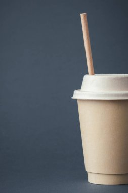 Coffee in a disposable paper cup with a straw on a gray background. Unbranded recycled paper cup with a copy space for a free text. Mockup. Care for the environment. Recycling or eco-friendly concept