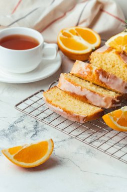 Loaf of orange bread covered with a confectionery glaze with lemon juice and decorated with orange slices. Chiffon cake on a pastry grill next to cup of tea. White background