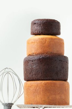 Freshly baked sponge biscuit on a pastry grid next to whisk, sieve for sifting flour and eggs. Brown chocolate and white vanilla sponge cake with professional confectioner utensils. White background