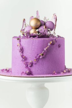 Wedding cake with violet cream cheese frosting decorated with caramel vase and golden chocolate spheres on the white background. Luxury anniversary cake on the white cake stand