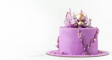Wedding cake with violet cream cheese frosting decorated with caramel vase and golden chocolate spheres on the white background. Luxury anniversary cake with pink chocolate velvet coating