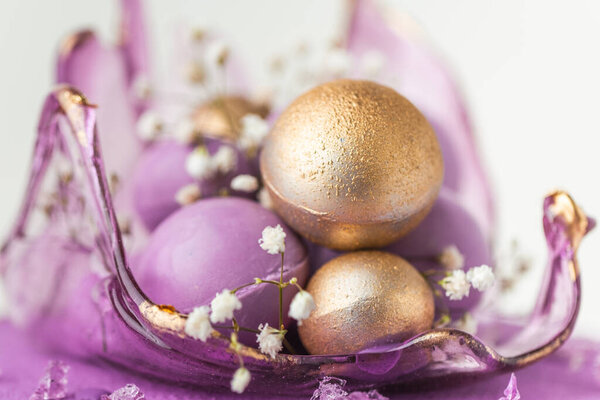 Свадебный торт с глазурью из сыра фиолетового крема, украшенный прозрачной карамельной вазой и золотыми шоколадными шарами на белом фоне. Макроснимок роскошного украшения торта годовщины