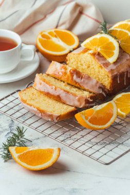 Loaf of orange bread covered with a confectionery glaze with lemon juice and decorated with orange slices. Chiffon cake on a pastry grill next to cup of tea. White background