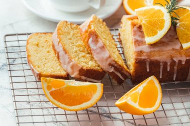 Loaf of orange bread covered with a confectionery glaze with lemon juice and decorated with orange slices. Chiffon cake on a pastry grill next to cup of tea. White background