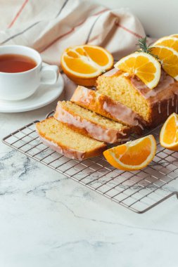 Loaf of orange bread covered with a confectionery glaze with lemon juice and decorated with orange slices. Chiffon cake on a pastry grill next to cup of tea. White background