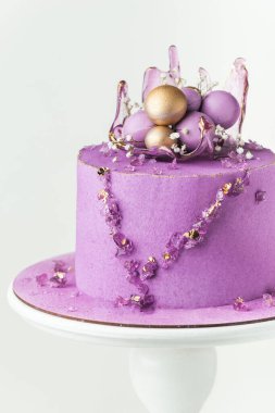 Wedding cake with violet cream cheese frosting decorated with caramel vase and golden chocolate spheres on the white background. Luxury anniversary cake on the white cake stand