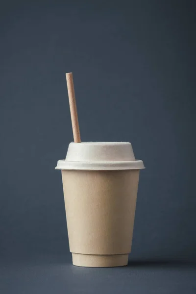 Coffee in a disposable paper cup with a straw on a gray background. Unbranded recycled paper cup with a copy space for a free text. Mockup. Care for the environment. Recycling or eco-friendly concept