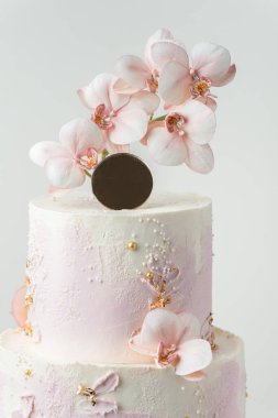 Wedding bunk cake with pink and white cream cheese frosting decorated with edible orchid sugar flowers and golden petals on the white background