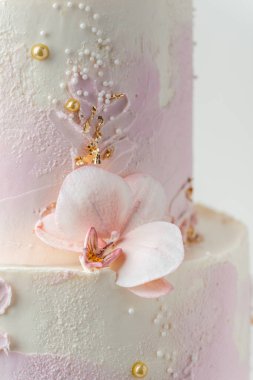 Close up of wedding bunk cake with pink and white cream cheese frosting decorated with edible orchid sugar flowers and golden petals on the white background