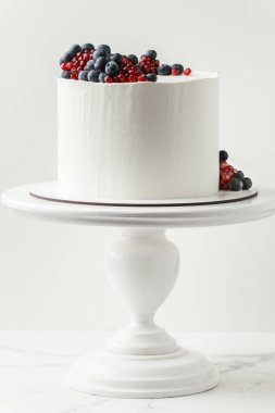 Birthday cake with white cream cheese frosting decorated with fresh blueberries and pomegranate. Elegant summer cake with red and blue berries on the white background