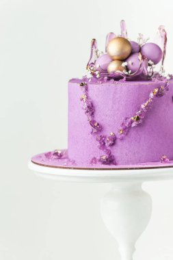 Wedding cake with violet cream cheese frosting decorated with caramel vase and golden chocolate spheres on the white background. Luxury anniversary cake on the white cake stand