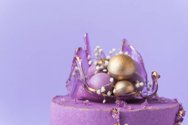 Wedding cake with violet cream cheese frosting decorated with caramel vase and golden chocolate spheres on the purple background. Luxury anniversary cake with pink chocolate velvet coating
