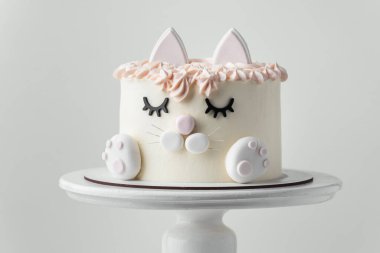 Cat cake for a little girl decorated with edible eyelids, ears and mastic paws on the white background. Birthday cake with white and pink cream cheese frosting