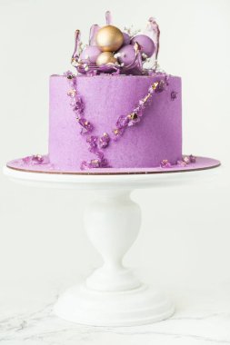 Wedding cake with violet cream cheese frosting decorated with caramel vase and golden chocolate spheres on the white background. Luxury anniversary cake on the white cake stand