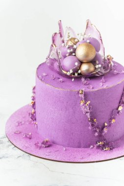 Wedding cake with violet cream cheese frosting decorated with caramel vase and golden chocolate spheres on the white background. Luxury anniversary cake with pink chocolate velvet coating