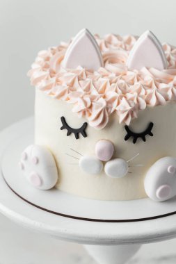 Cat cake for a little girl decorated with edible eyelids, ears and mastic paws on the white background. Birthday cake with white and pink cream cheese frosting