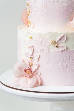 Close up of wedding bunk cake with pink and white cream cheese frosting decorated with edible orchid sugar flowers and golden petals on the white background