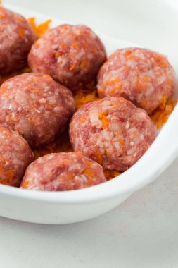 Homemade meatballs with tomato sauce, carrot and spices. Raw ground beef meatballs with rice in a white dish for baking. White marble background. Original way to cook meat