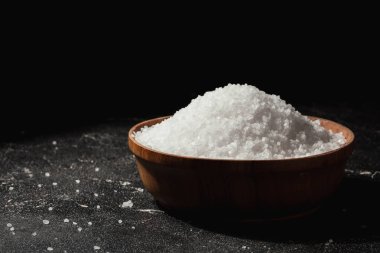Coarse white salt in a wooden bowl on the black background