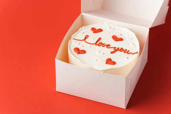 Korean style bento cake in a white gift box on the red festive background. Little cake with I love you inscription. Happy Valentine\'s Day
