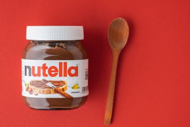 KYIV, UKRAINE - 21 Şubat: Nutella çikolatalı fındık, cam bir kavanoza serpilmiş, yanında beyaz kaşık ve kırmızı fındık var. Üst Manzara. Boşluğu kopyala.